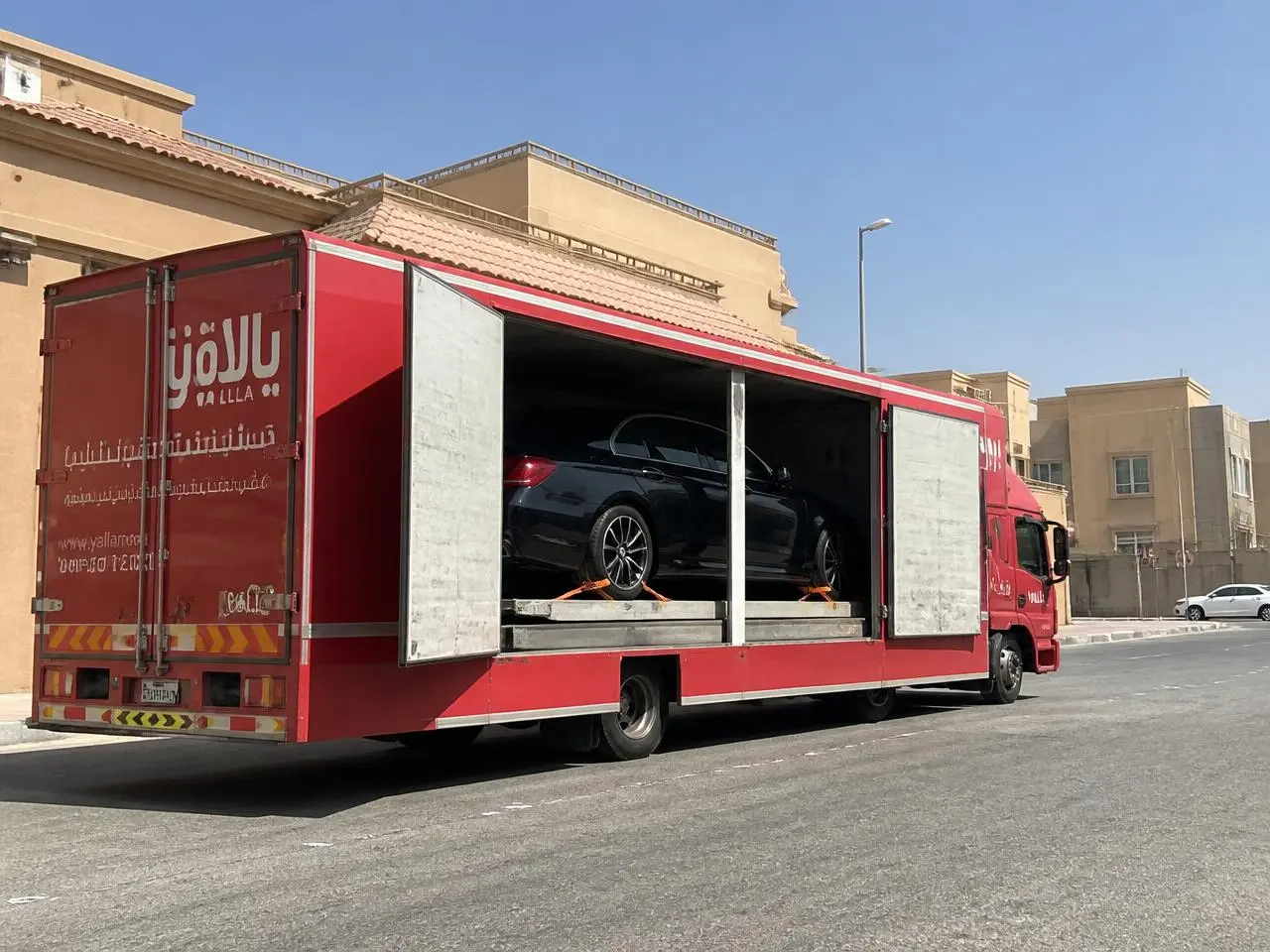 سطحة مغلقة بأبواب جانبية مفتوحة تنقل سيارة فاخرة داخل حي سكني